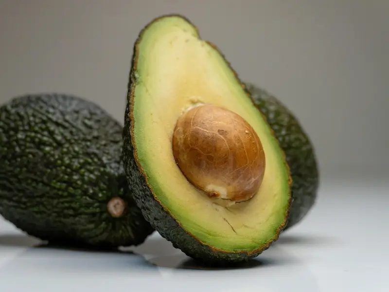 Un aguacate entero y otro partido por la mitad con su hueso