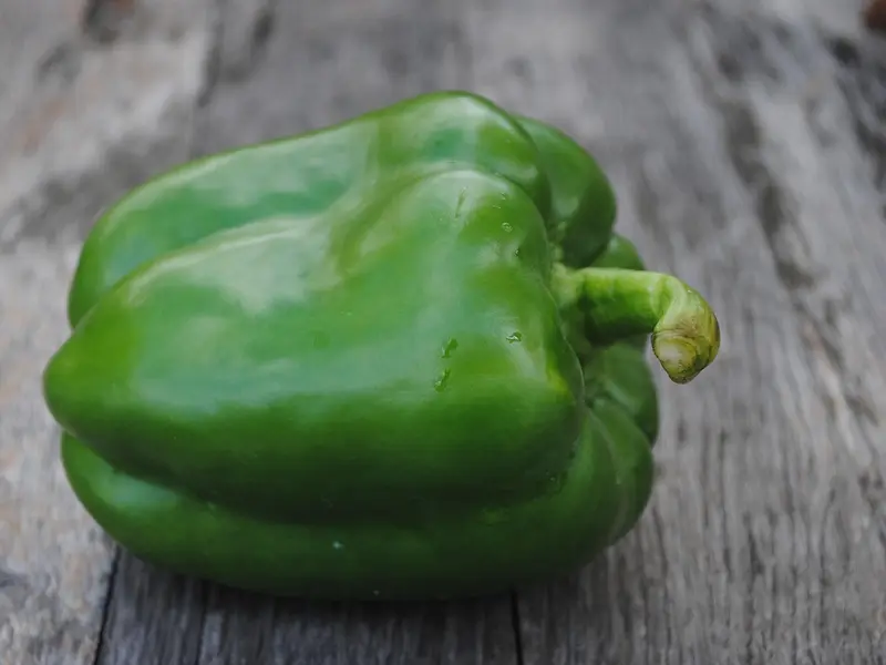 Pimiento verde entero sobre una mesa de madera